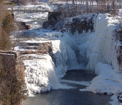 [Several small falls close to each other but at different heights pouring into the Ausable River. Most of the edges of the falls are frozen.]